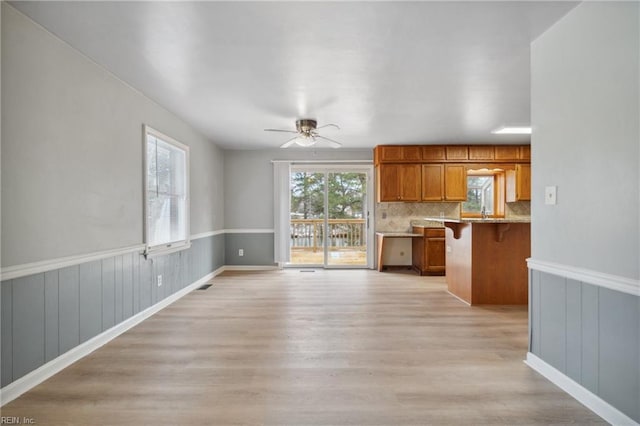 kitchen featuring a breakfast bar, light wood-type flooring, kitchen peninsula, ceiling fan, and backsplash