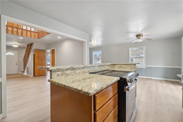 kitchen featuring stainless steel electric range, ceiling fan, a center island, light stone countertops, and light wood-type flooring