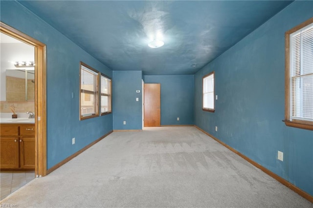 unfurnished bedroom featuring ensuite bath, sink, and light carpet