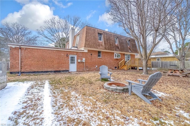 snow covered back of property with a wooden deck and an outdoor fire pit