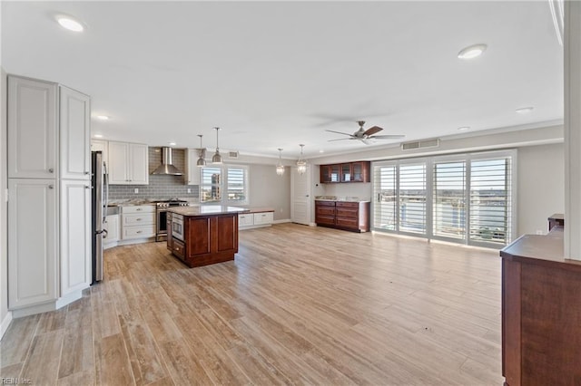 kitchen with white cabinetry, decorative light fixtures, a center island, appliances with stainless steel finishes, and wall chimney range hood