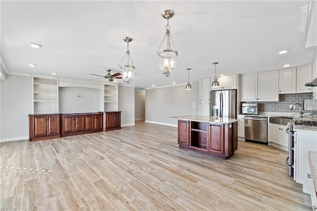 kitchen with hanging light fixtures, stainless steel appliances, a center island, ornamental molding, and white cabinets