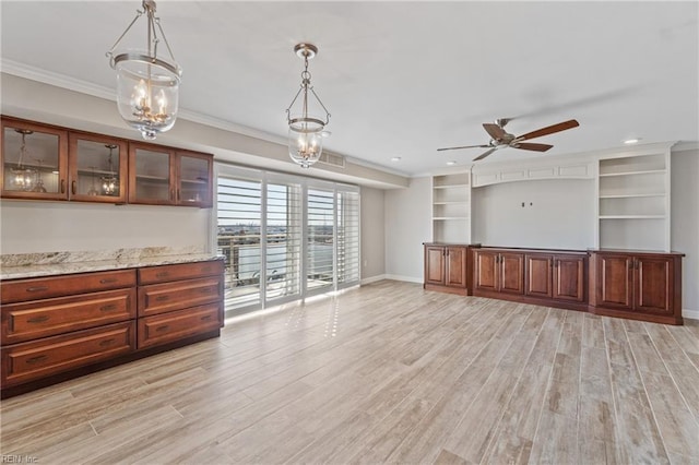 interior space with ornamental molding, light stone countertops, decorative light fixtures, and light hardwood / wood-style flooring