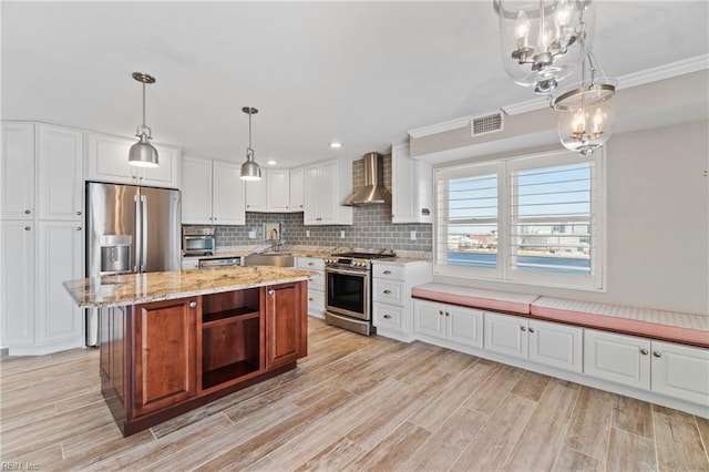 kitchen featuring wall chimney exhaust hood, a center island, appliances with stainless steel finishes, pendant lighting, and white cabinets