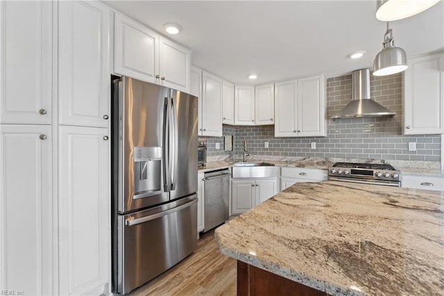 kitchen with wall chimney range hood, appliances with stainless steel finishes, white cabinetry, light stone countertops, and decorative light fixtures