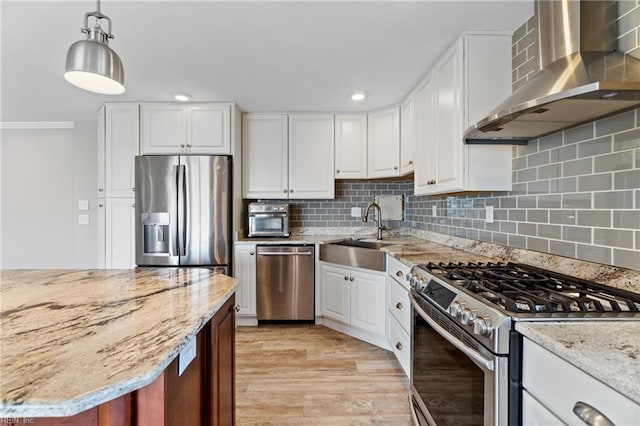 kitchen featuring wall chimney range hood, stainless steel appliances, sink, and white cabinets