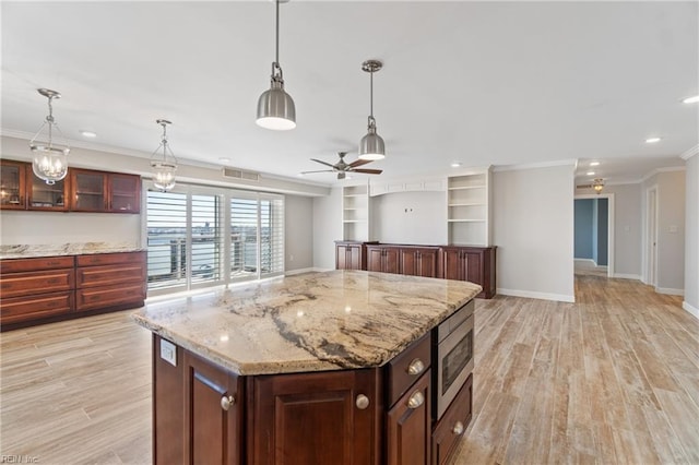 kitchen featuring stainless steel microwave, hanging light fixtures, light hardwood / wood-style flooring, and a center island