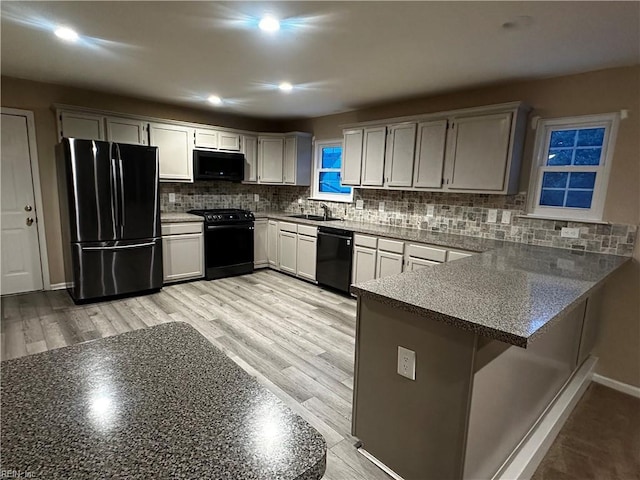 kitchen featuring sink, backsplash, light hardwood / wood-style floors, black appliances, and kitchen peninsula