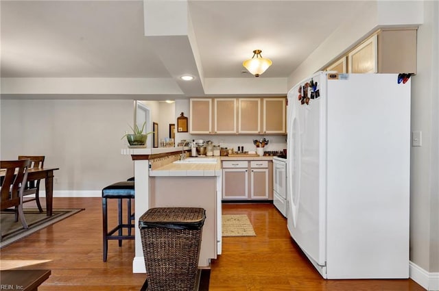 kitchen featuring sink, white appliances, a kitchen breakfast bar, light hardwood / wood-style floors, and kitchen peninsula