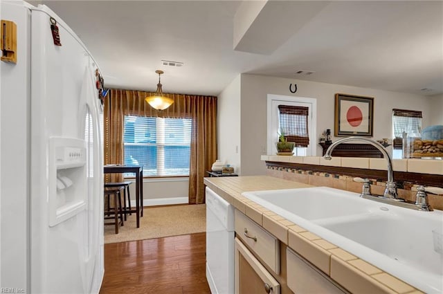 kitchen featuring dark wood-type flooring, sink, tile countertops, pendant lighting, and white appliances