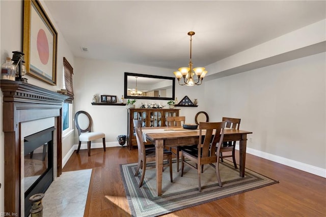 dining area with dark hardwood / wood-style floors, a premium fireplace, and an inviting chandelier