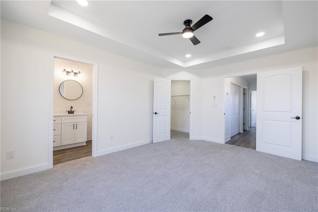 unfurnished bedroom with ensuite bathroom, sink, a tray ceiling, ceiling fan, and carpet