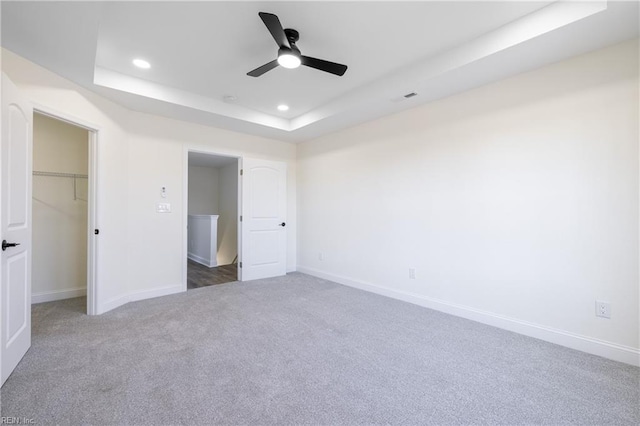 unfurnished bedroom with a closet, a spacious closet, ceiling fan, and a tray ceiling