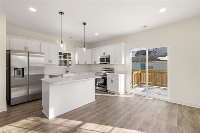 kitchen with a kitchen island, appliances with stainless steel finishes, white cabinetry, wood-type flooring, and hanging light fixtures