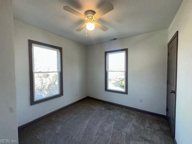 empty room with ceiling fan, a wealth of natural light, and dark colored carpet