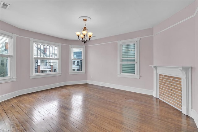 unfurnished living room with wood-type flooring, a fireplace, and a notable chandelier