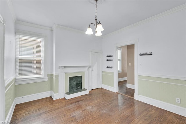 unfurnished living room with a tiled fireplace, crown molding, wood-type flooring, and a notable chandelier