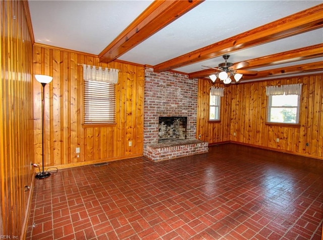 unfurnished living room featuring ceiling fan, a fireplace, wooden walls, and beamed ceiling