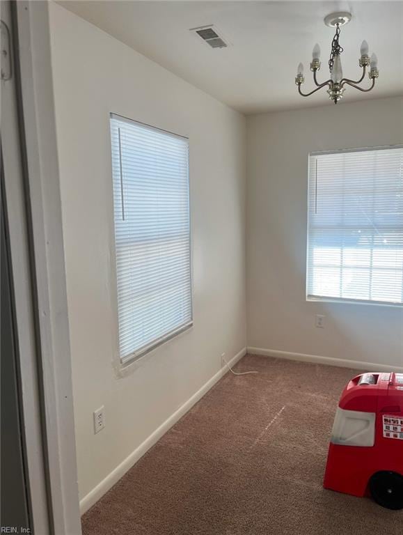 carpeted empty room with an inviting chandelier