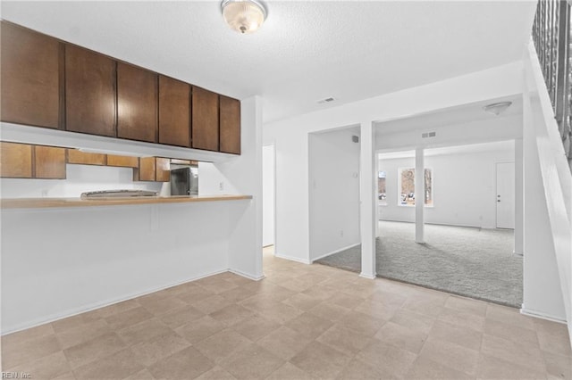 kitchen featuring light colored carpet, a kitchen breakfast bar, refrigerator, and kitchen peninsula