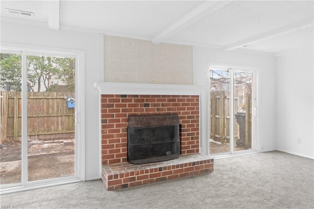 unfurnished living room with a brick fireplace, carpet floors, beamed ceiling, and plenty of natural light