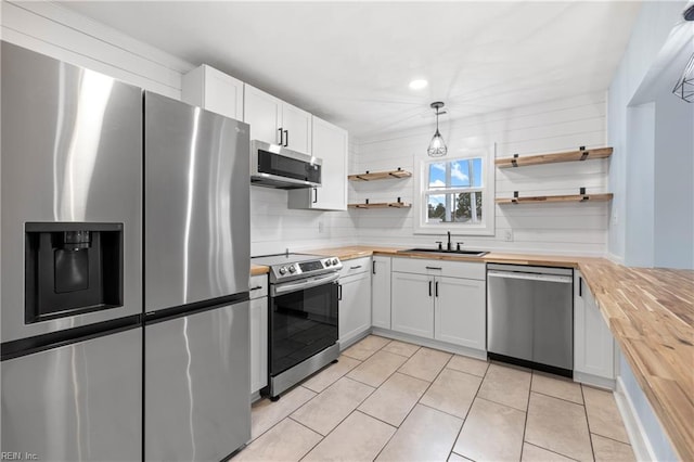 kitchen with appliances with stainless steel finishes, pendant lighting, butcher block countertops, white cabinetry, and sink