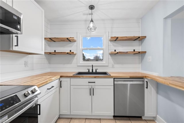 kitchen with hanging light fixtures, appliances with stainless steel finishes, white cabinets, and butcher block countertops