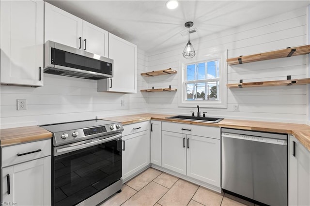 kitchen with appliances with stainless steel finishes, decorative light fixtures, white cabinetry, sink, and wooden counters