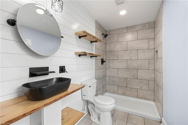 bathroom with tile patterned flooring, vanity, a tile shower, and toilet