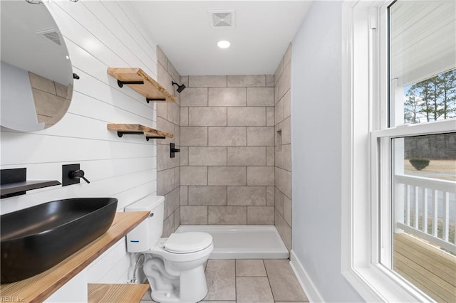 bathroom with toilet, sink, a tile shower, a wealth of natural light, and tile patterned flooring