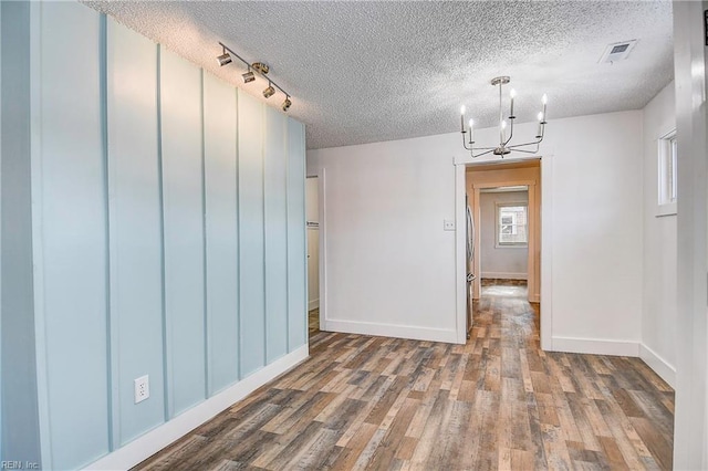 empty room featuring a textured ceiling, dark hardwood / wood-style floors, and a chandelier