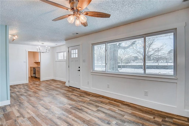 entrance foyer with ceiling fan with notable chandelier, a textured ceiling, and light hardwood / wood-style flooring