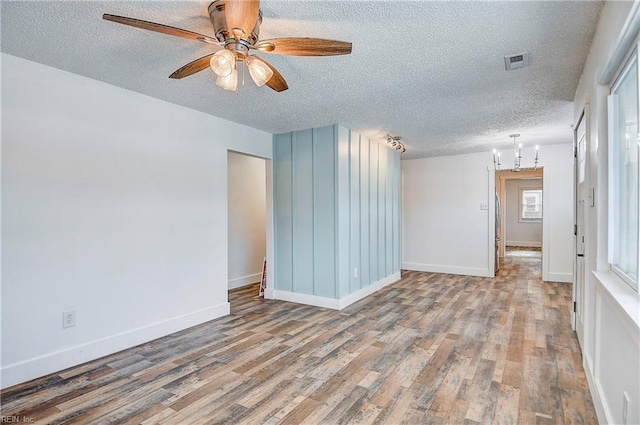 empty room with hardwood / wood-style flooring, ceiling fan with notable chandelier, and a textured ceiling