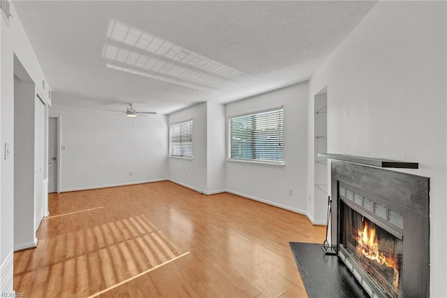 unfurnished living room with ceiling fan, built in features, a textured ceiling, and light hardwood / wood-style floors