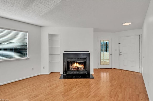 unfurnished living room with wood-type flooring, built in features, and a textured ceiling