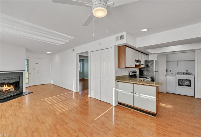 kitchen with stone counters, washing machine and dryer, appliances with stainless steel finishes, and light hardwood / wood-style floors