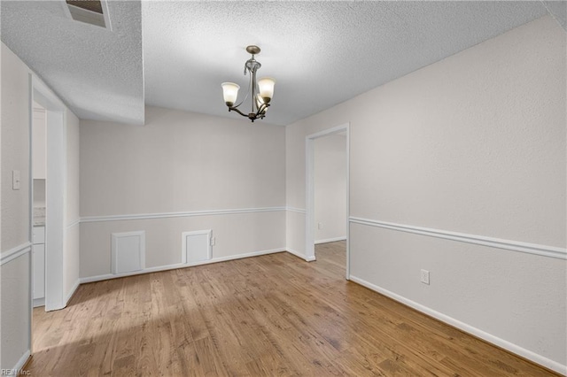 spare room featuring an inviting chandelier, light hardwood / wood-style flooring, and a textured ceiling