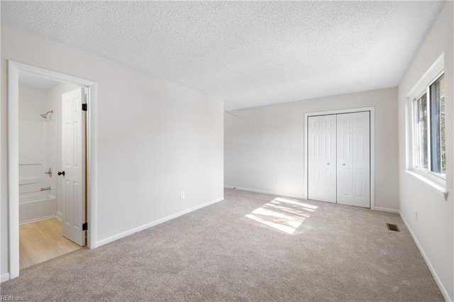 unfurnished bedroom featuring ensuite bath, light colored carpet, a closet, and a textured ceiling