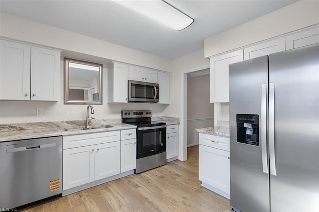 kitchen featuring sink, white cabinets, stainless steel appliances, light stone countertops, and light wood-type flooring