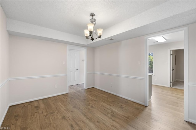 empty room featuring hardwood / wood-style floors, a textured ceiling, a raised ceiling, and a chandelier