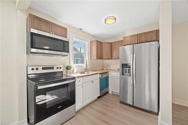 kitchen with appliances with stainless steel finishes, light hardwood / wood-style floors, sink, and white cabinets