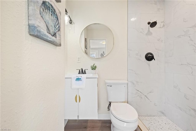 bathroom with hardwood / wood-style floors, vanity, a tile shower, and toilet