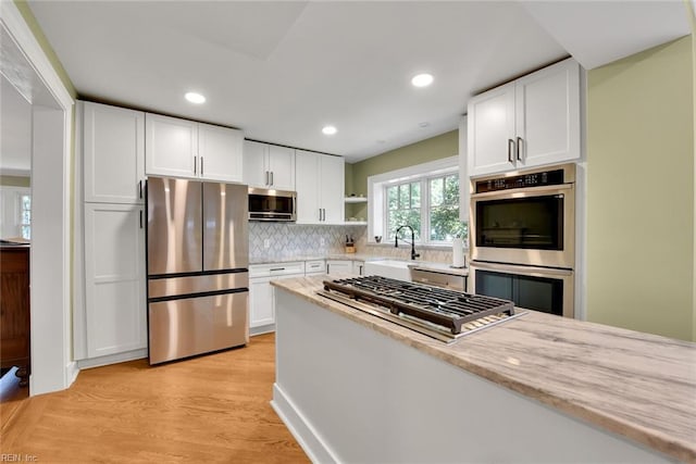 kitchen with white cabinetry, sink, light stone counters, stainless steel appliances, and light wood-type flooring