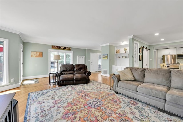 living room with ornamental molding, a barn door, and light wood-type flooring