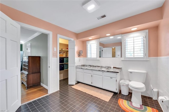 bathroom featuring tile patterned floors, toilet, crown molding, tile walls, and vanity