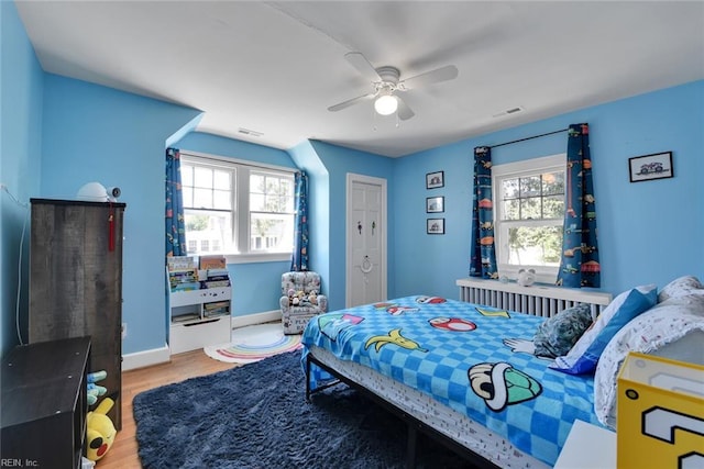 bedroom with ceiling fan, wood-type flooring, and multiple windows