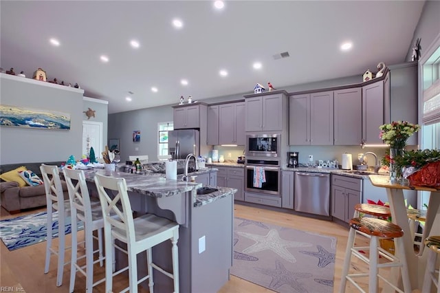 kitchen featuring a kitchen bar, sink, appliances with stainless steel finishes, stone counters, and a kitchen island with sink