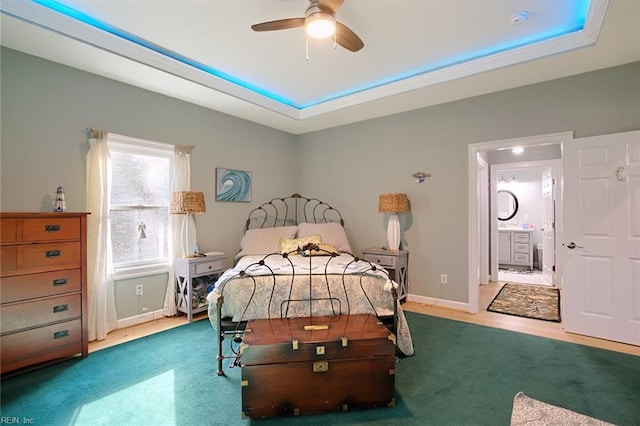 bedroom with a raised ceiling, connected bathroom, light colored carpet, and ceiling fan