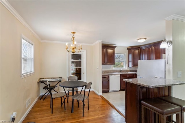 kitchen with sink, light stone counters, hanging light fixtures, light wood-type flooring, and white appliances