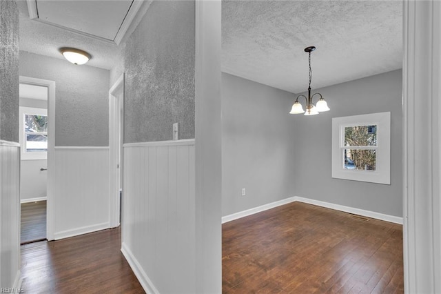 unfurnished dining area with dark hardwood / wood-style floors, a chandelier, and a textured ceiling